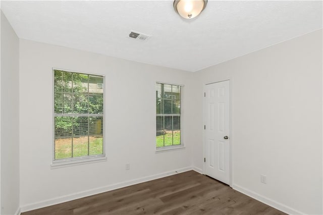 unfurnished room with dark wood-style floors, visible vents, and baseboards