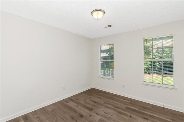 unfurnished room with dark wood-style floors, plenty of natural light, visible vents, and baseboards