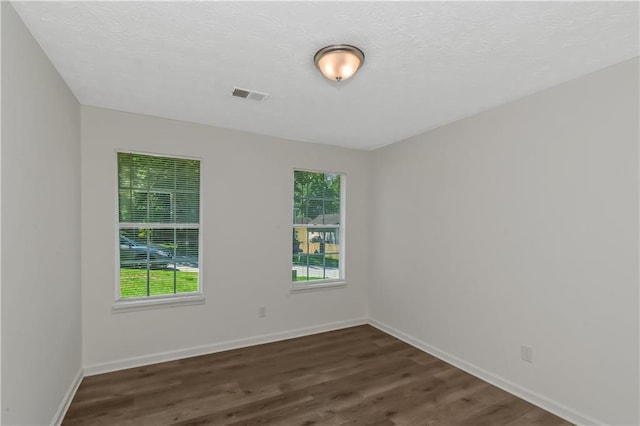 empty room featuring a healthy amount of sunlight, baseboards, visible vents, and dark wood-type flooring