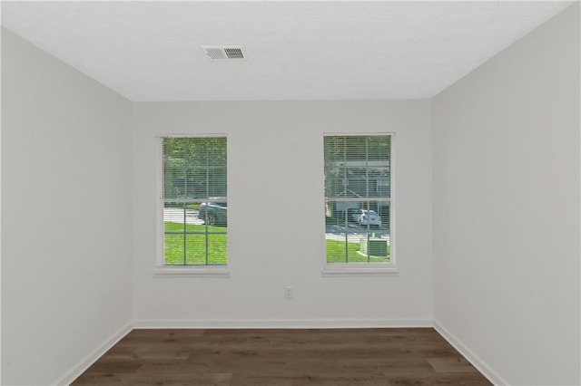 empty room featuring dark wood-type flooring, a wealth of natural light, visible vents, and baseboards