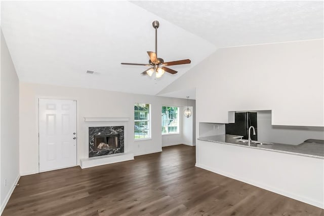 unfurnished living room with dark wood-style floors, lofted ceiling, a premium fireplace, a ceiling fan, and baseboards