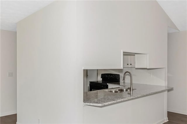 kitchen with electric range, baseboards, light stone countertops, white cabinetry, and a sink