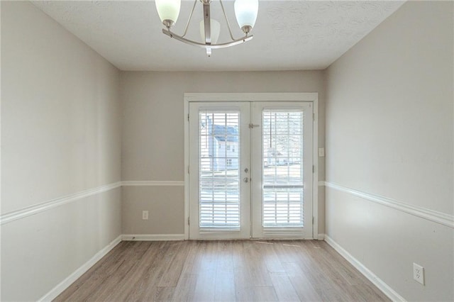 empty room featuring light wood finished floors, baseboards, french doors, a notable chandelier, and a textured ceiling