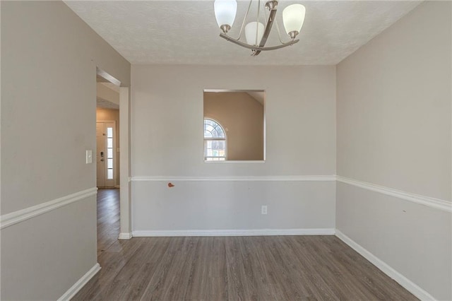 empty room with a notable chandelier, wood finished floors, baseboards, and a textured ceiling