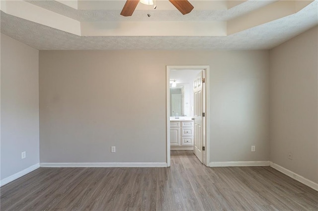 spare room featuring wood finished floors, baseboards, ceiling fan, a textured ceiling, and a raised ceiling