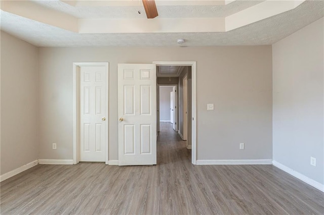 unfurnished bedroom featuring attic access, wood finished floors, baseboards, and a textured ceiling