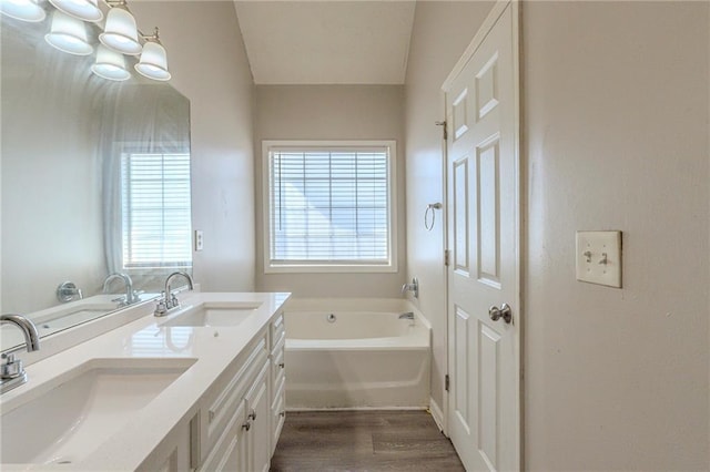 full bath with a sink, wood finished floors, double vanity, and a bath