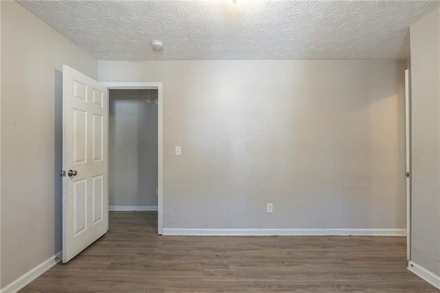 empty room with baseboards, a textured ceiling, and wood finished floors