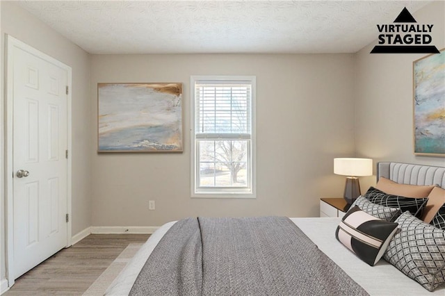 bedroom featuring baseboards, a textured ceiling, and wood finished floors