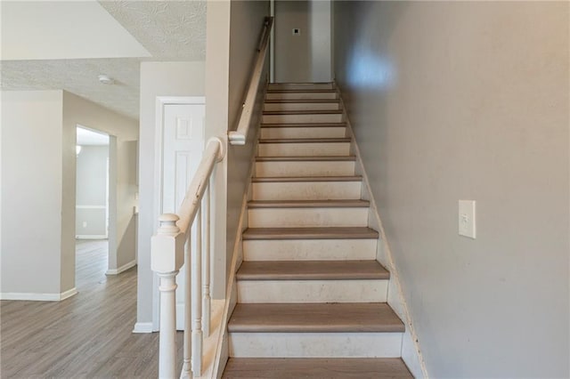 stairway with baseboards, a textured ceiling, and wood finished floors