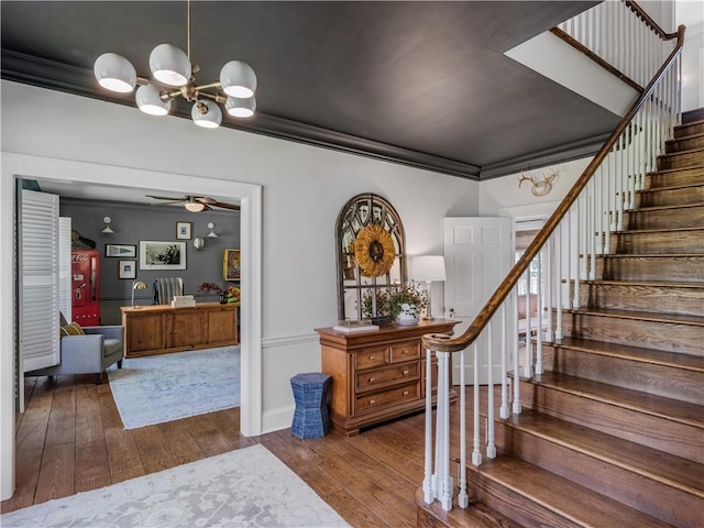 staircase with crown molding, ceiling fan with notable chandelier, and hardwood / wood-style floors