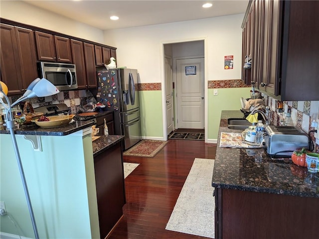 kitchen featuring appliances with stainless steel finishes, dark brown cabinetry, dark stone counters, and sink