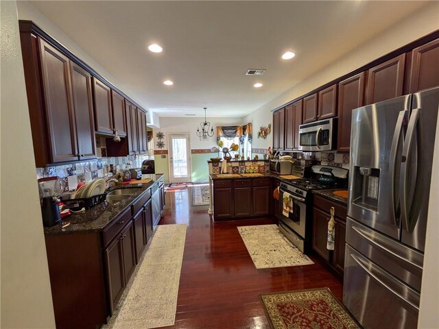 kitchen featuring dark wood-type flooring, stainless steel appliances, dark stone countertops, sink, and kitchen peninsula