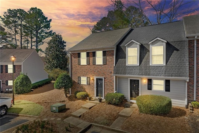 view of front of property featuring brick siding and roof with shingles