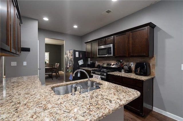 kitchen featuring sink, appliances with stainless steel finishes, dark brown cabinets, tasteful backsplash, and light stone countertops