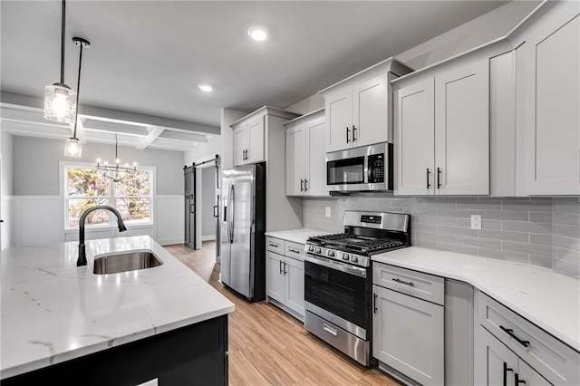 kitchen with sink, hanging light fixtures, stainless steel appliances, a barn door, and light hardwood / wood-style flooring