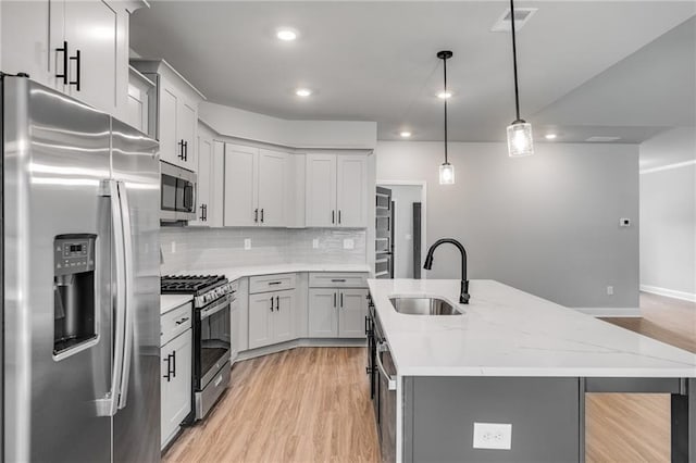 kitchen featuring pendant lighting, sink, stainless steel appliances, light stone countertops, and a center island with sink