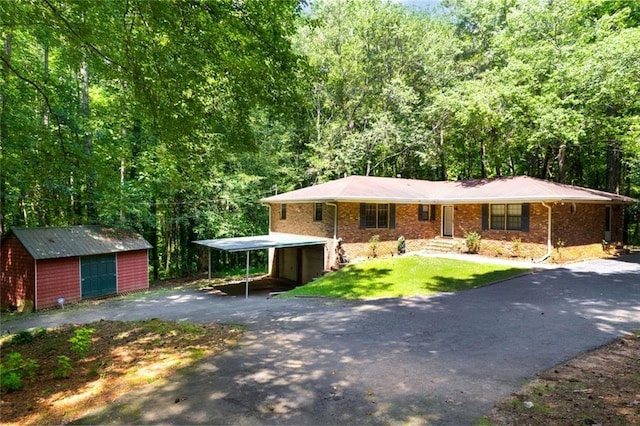 view of front of property featuring a forest view, aphalt driveway, a detached carport, and a front lawn