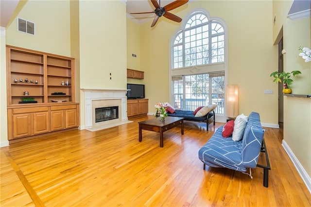 living room with a towering ceiling, ornamental molding, ceiling fan, and light hardwood / wood-style flooring