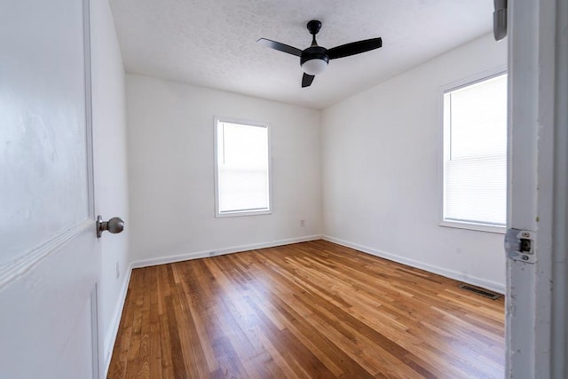 empty room featuring a wealth of natural light, a textured ceiling, baseboards, and wood-type flooring