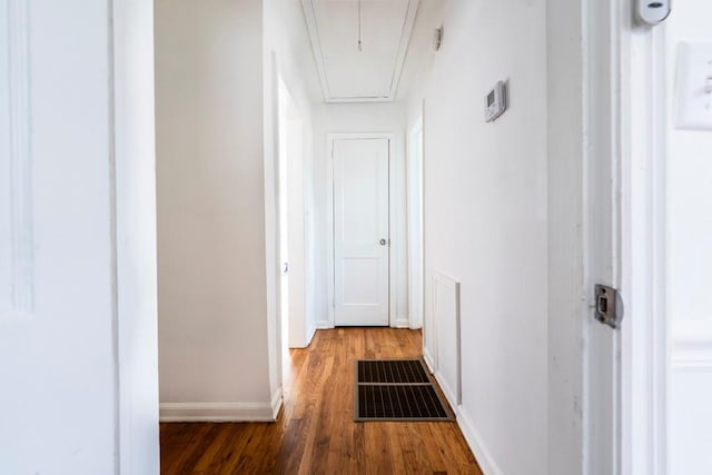 hall with visible vents, baseboards, attic access, and wood finished floors