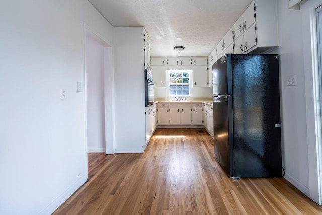 kitchen featuring light wood-type flooring, black appliances, a sink, white cabinetry, and light countertops