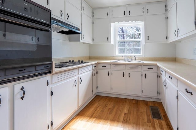 kitchen featuring visible vents, a sink, light wood-style floors, electric cooktop, and under cabinet range hood