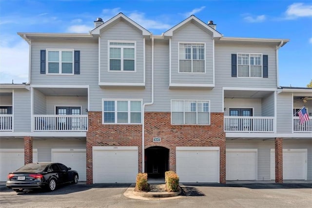 townhome / multi-family property with a garage, driveway, a chimney, and brick siding