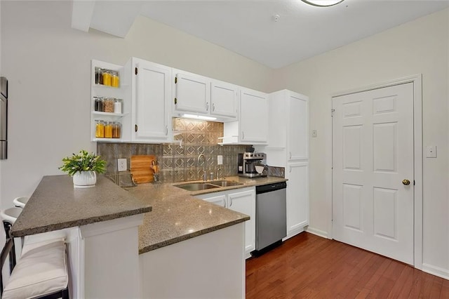 kitchen with backsplash, stainless steel dishwasher, white cabinetry, a sink, and a peninsula