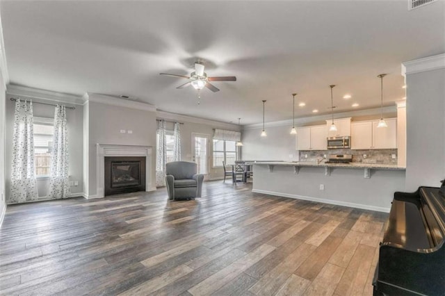 living room with a ceiling fan, ornamental molding, dark wood finished floors, a glass covered fireplace, and recessed lighting
