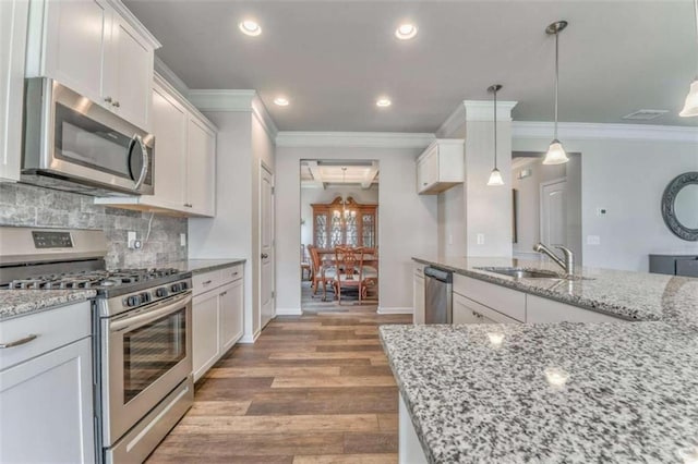 kitchen with appliances with stainless steel finishes, a sink, ornamental molding, light wood-style floors, and baseboards