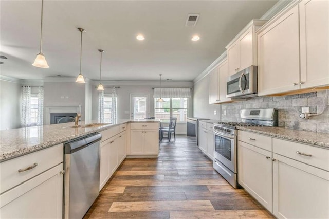 kitchen featuring stainless steel appliances, crown molding, wood finished floors, decorative backsplash, and pendant lighting