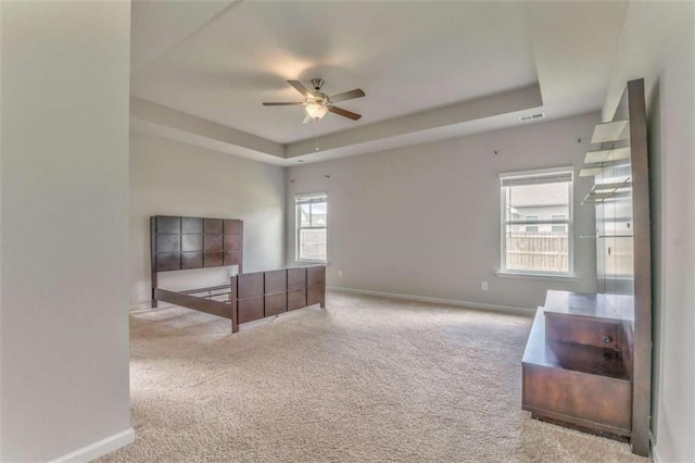 unfurnished bedroom with a tray ceiling, carpet flooring, baseboards, and ceiling fan