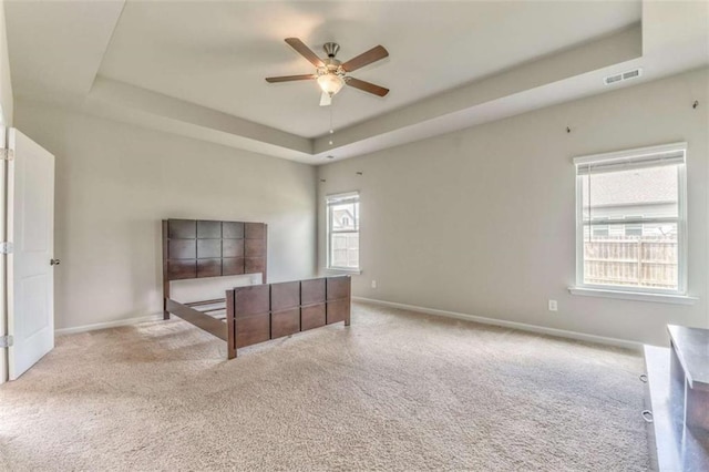 carpeted bedroom featuring a tray ceiling, multiple windows, and baseboards