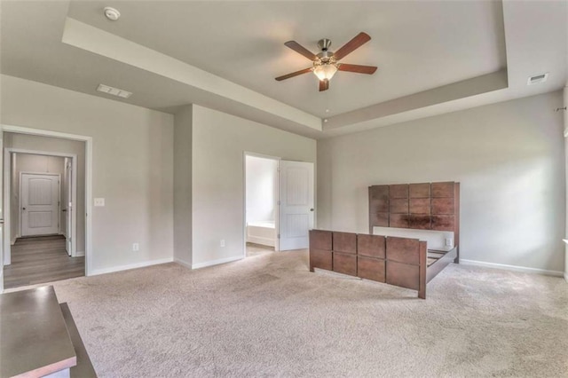 unfurnished living room with a raised ceiling, a ceiling fan, baseboards, and carpet