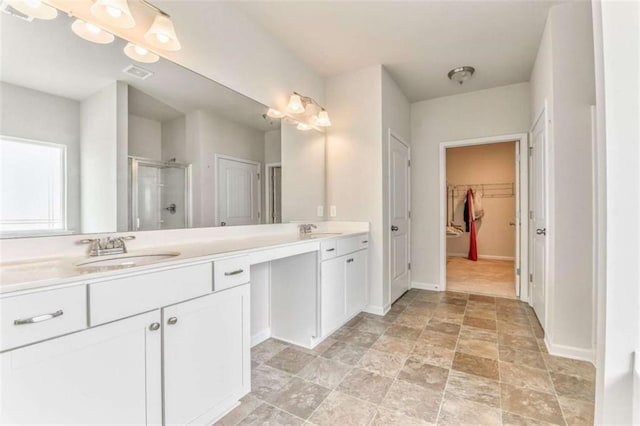 full bathroom featuring a shower stall, double vanity, a spacious closet, baseboards, and stone finish floors