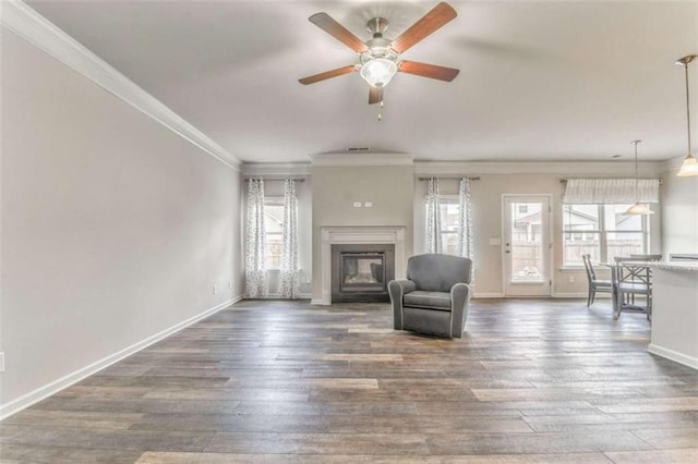 living room with healthy amount of natural light, a ceiling fan, a glass covered fireplace, baseboards, and ornamental molding