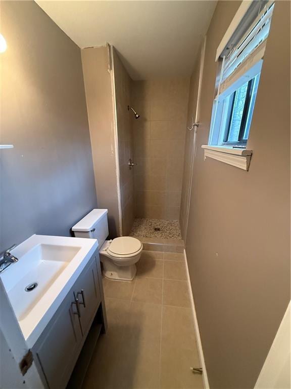 bathroom with toilet, a tile shower, vanity, and tile patterned floors