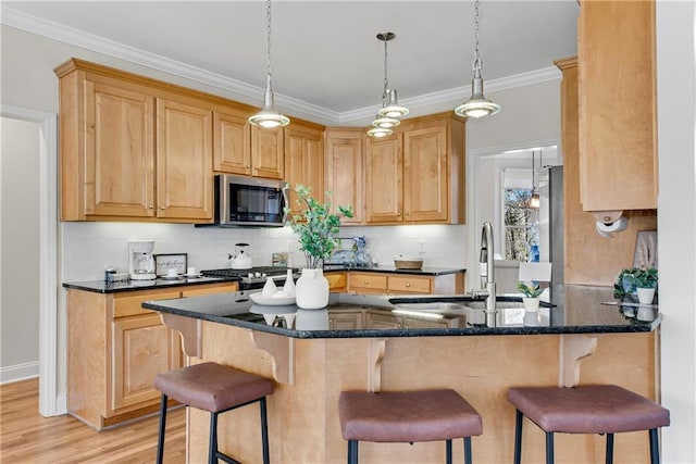 kitchen featuring appliances with stainless steel finishes, a kitchen bar, dark stone counters, ornamental molding, and kitchen peninsula