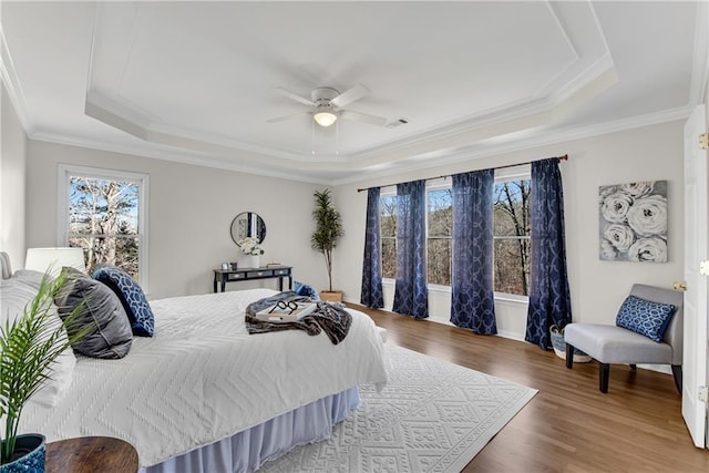 bedroom with a raised ceiling, wood-type flooring, and multiple windows