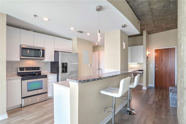 kitchen featuring hanging light fixtures, white cabinets, light hardwood / wood-style floors, and appliances with stainless steel finishes