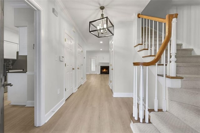 foyer entrance featuring light wood-type flooring, crown molding, and an inviting chandelier