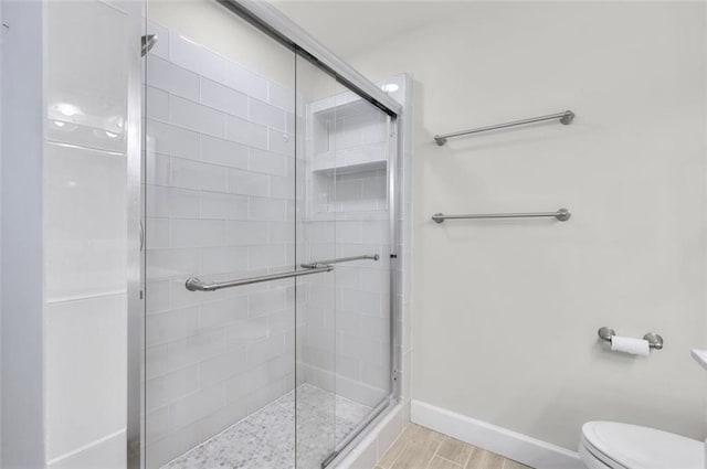 bathroom featuring toilet, an enclosed shower, and wood-type flooring