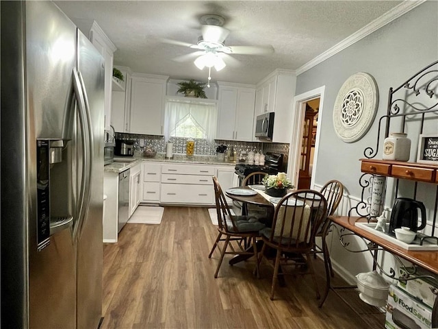 kitchen featuring white cabinets, ornamental molding, tasteful backsplash, wood-type flooring, and stainless steel appliances