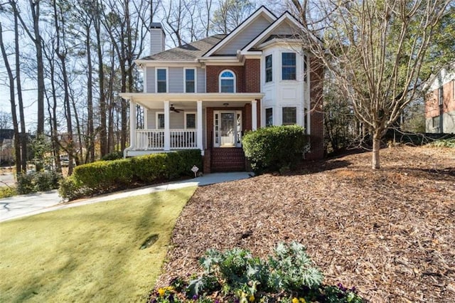 view of front of property with brick siding, a chimney, a porch, a ceiling fan, and a front lawn