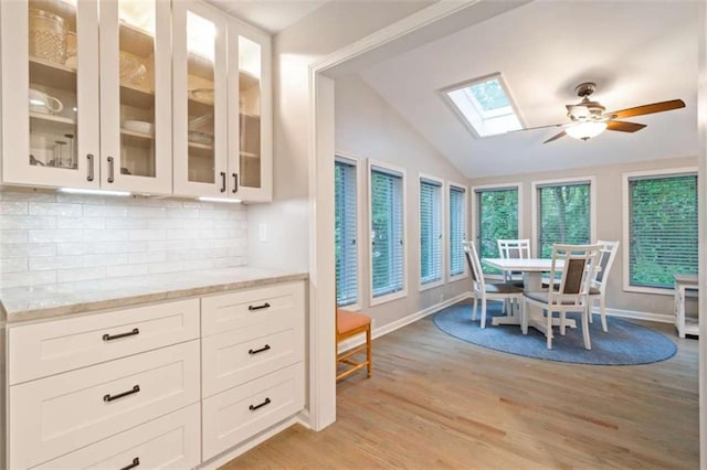 dining space featuring vaulted ceiling with skylight, baseboards, light wood-style flooring, and a ceiling fan