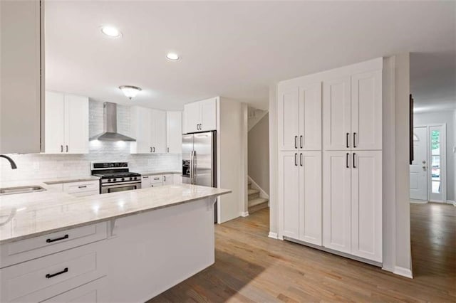 kitchen with light stone counters, a sink, appliances with stainless steel finishes, wall chimney exhaust hood, and tasteful backsplash