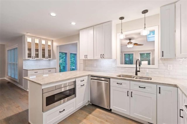 kitchen with stainless steel appliances, a peninsula, a sink, and white cabinetry