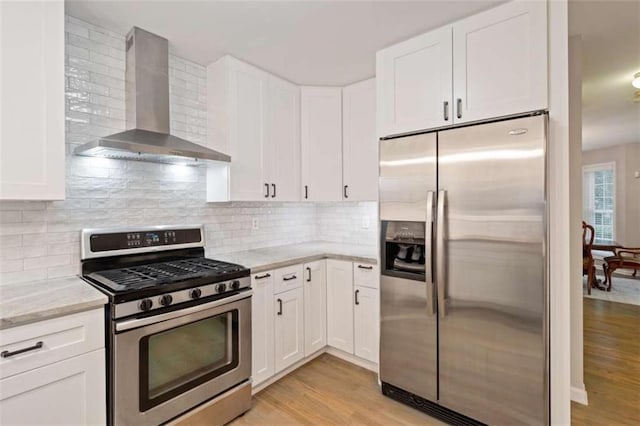 kitchen with white cabinets, wall chimney exhaust hood, appliances with stainless steel finishes, and light wood-style flooring