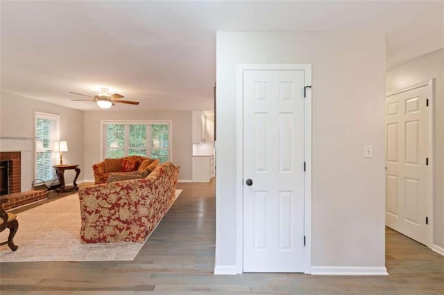 living room with ceiling fan, a fireplace, baseboards, and wood finished floors